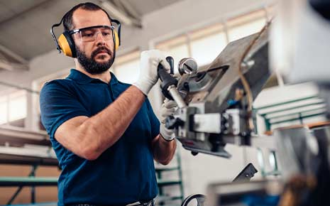 man with ear and eye protection working on cnc lathe machine