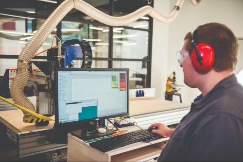 male employee wearing hearing protection sits at computer work station monitoring an automated machine