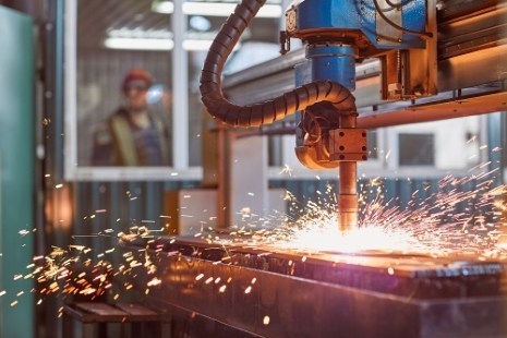 laser cutter in action, sparks flying, and an operator watching behind a glass enclosure