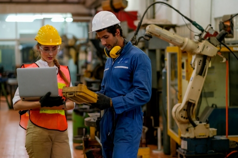 woman in a safety vest and hard hat discussing work with a man in overalls and ppe